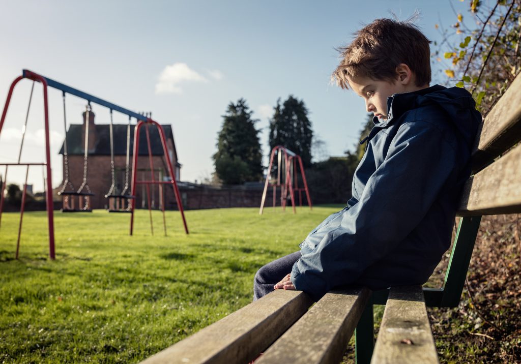 Upset problem child sitting on play park playground bench concep