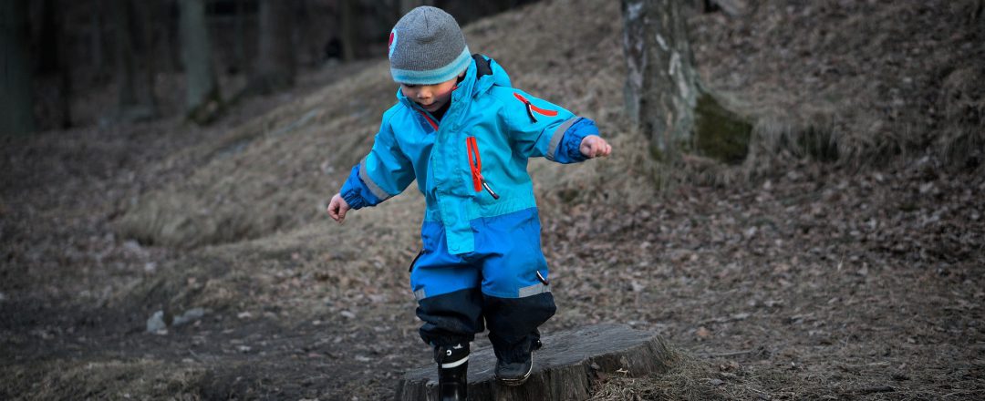 Young boy taking a leap off of a tree trunk