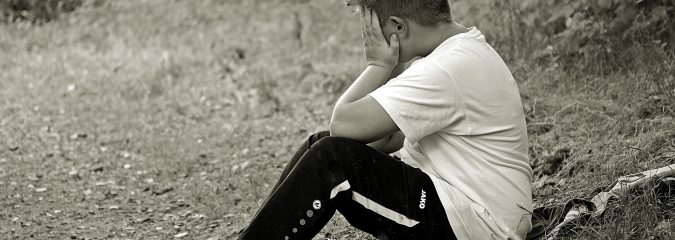 Boy sitting on the ground holding his head in grief